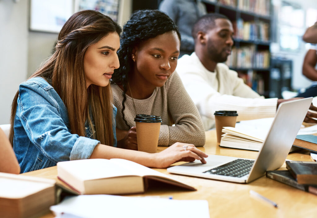 Shot of two young women using a laptop together in a college library.